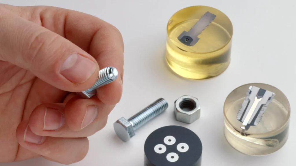 Metallurgist holding a bolt, in front of metallographic mounts of bolts and hardware