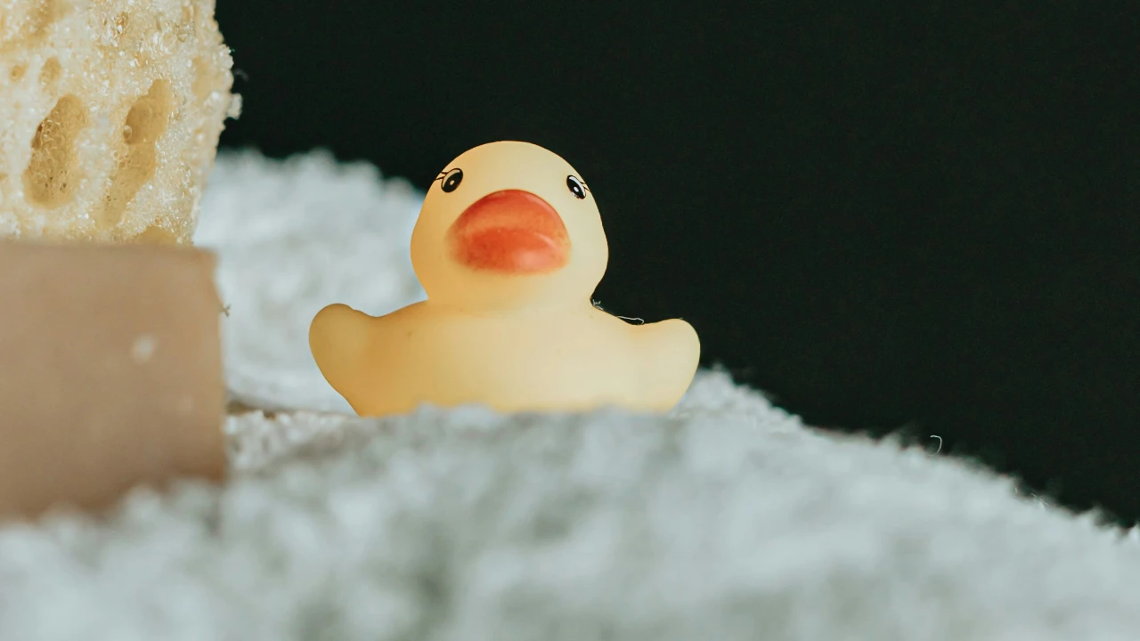 Rubber duck on a bat towel next with sponge and soap